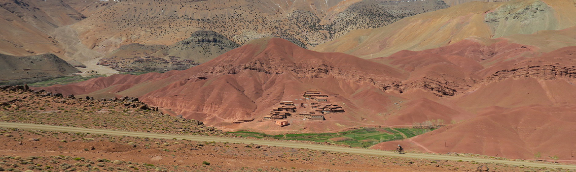 Ciclista su pista sterrata circondata dal tipico terreno ocra dell'Atlante marocchino